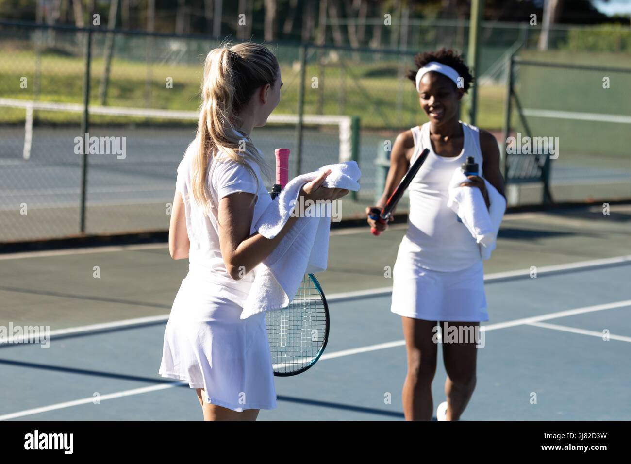 Souriante femme multiraciale joueurs avec une serviette parlant pendant la pause sur le court de tennis le jour ensoleillé Banque D'Images