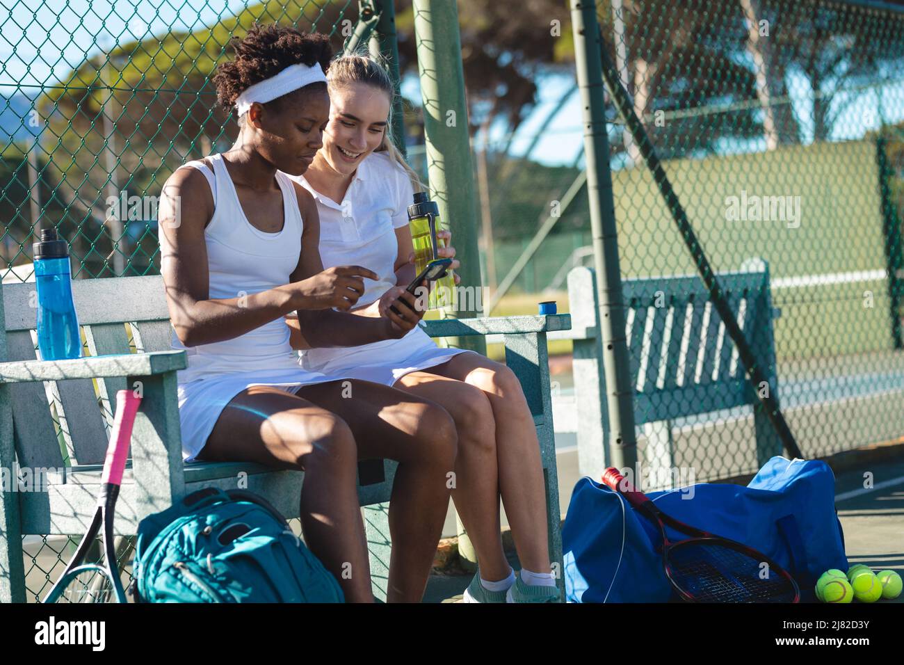 Jeunes femmes souriantes et multiraciales qui partagent leur smartphone sur le banc pendant la pause Banque D'Images