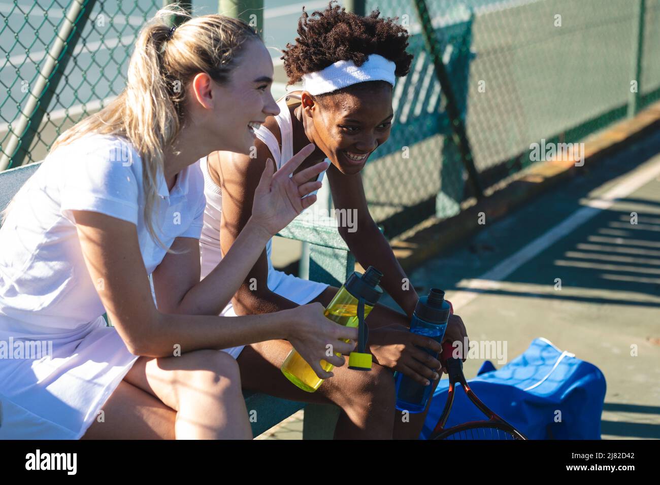 De jeunes joueuses de tennis multiraciales joyeuses, en train de faire une pause tout en parlant sur le court par beau temps Banque D'Images