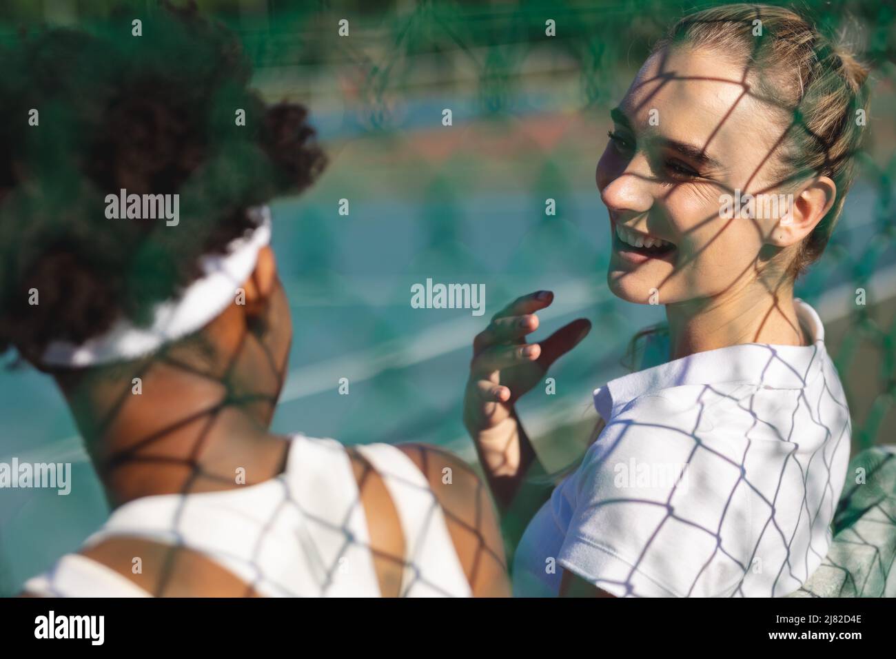 Bonne joueuse de tennis caucasienne discutant avec une athlète afro-américaine pendant la pause sur le terrain Banque D'Images
