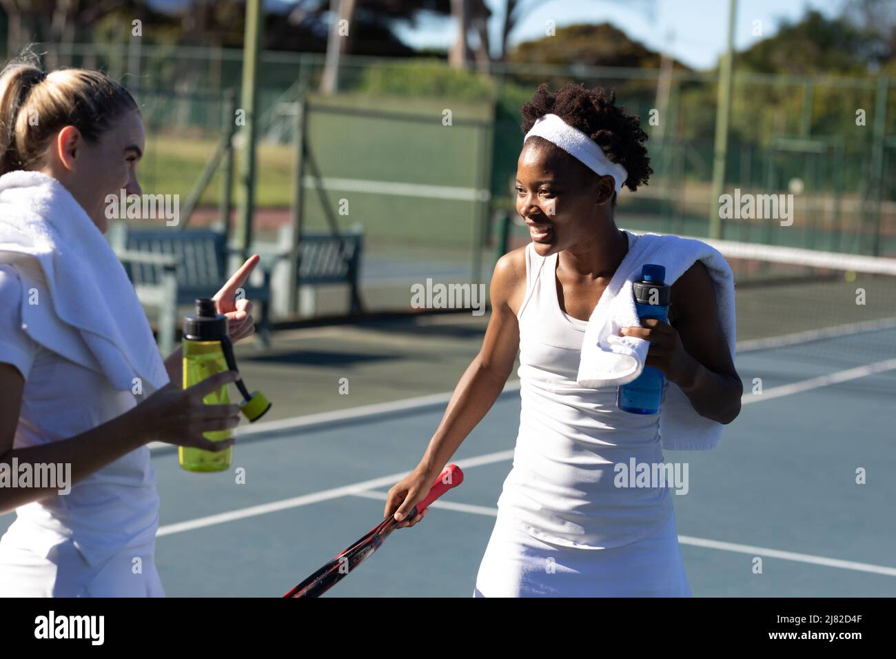 Des joueuses de tennis biraciales ravie de parler tout en profitant d'une pause sur le court par beau temps Banque D'Images