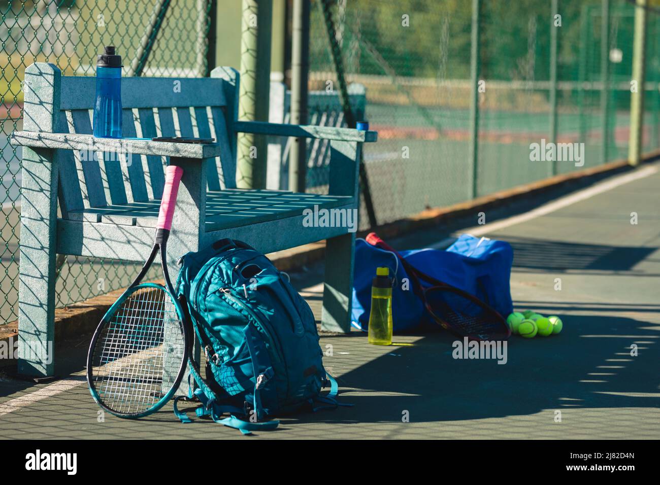 Raquette de tennis avec sacs à dos et bouteilles sur banc en bois vide sur le court par beau temps Banque D'Images