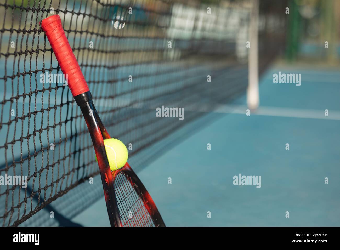 Balle de tennis et raquette rouge penchée sur le filet sur le court par beau temps Banque D'Images