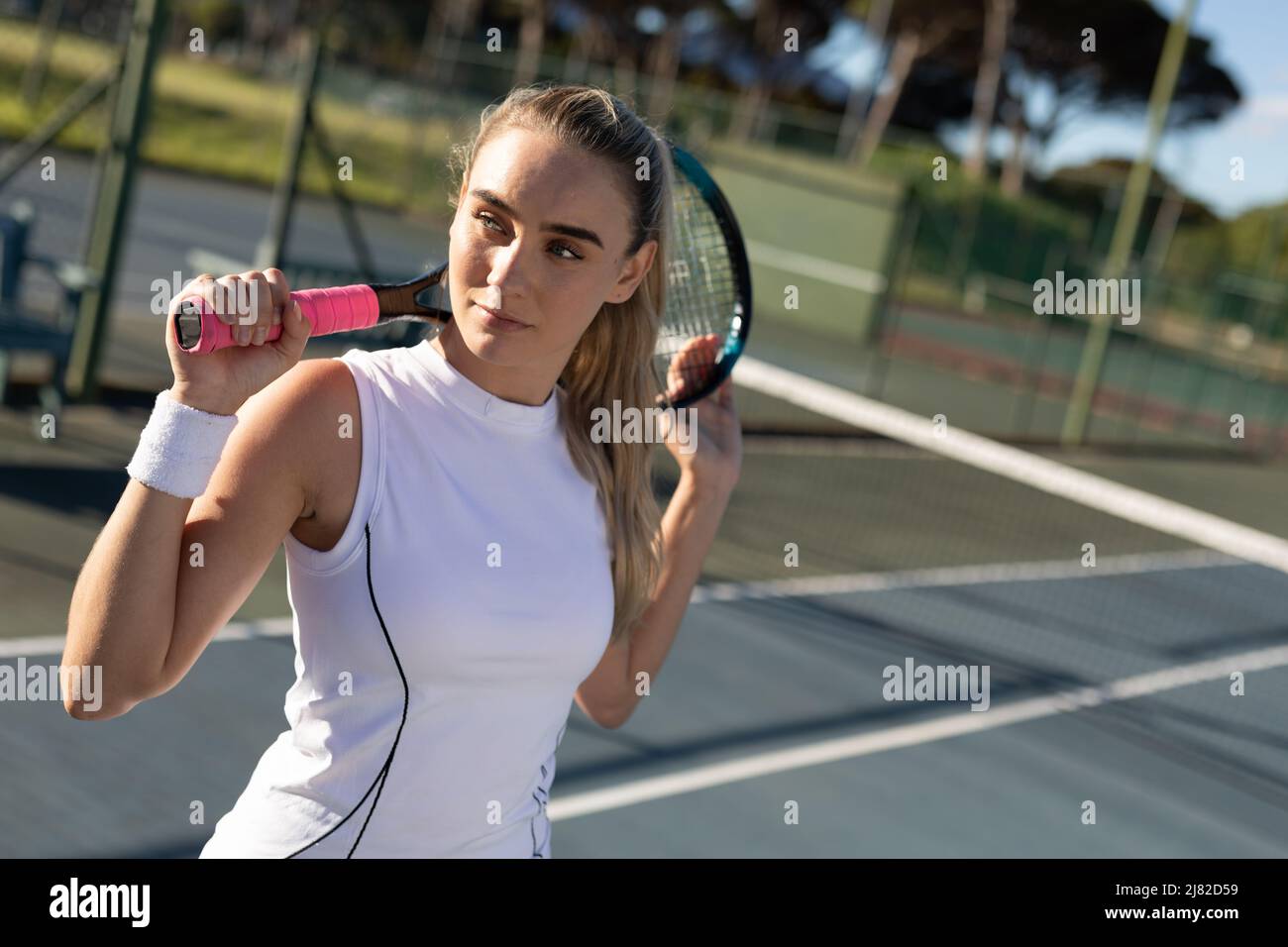 Belle jeune femme de tennis caucasien avec raquette derrière la tête en regardant loin sur le court Banque D'Images