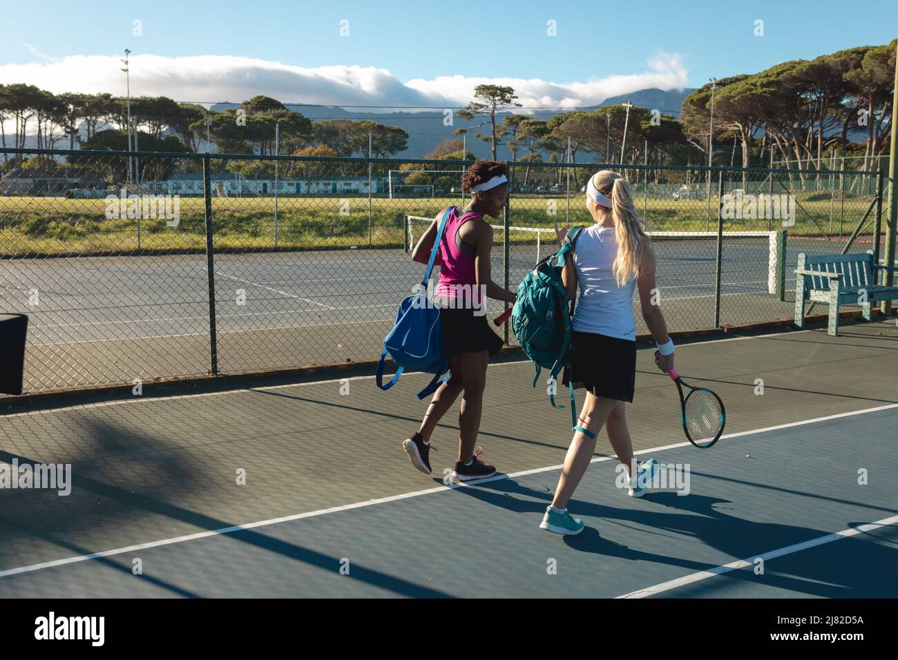 Une longueur complète de joueuses de tennis multiraciales marchant avec des raquettes et des sacs sur le terrain par beau temps Banque D'Images