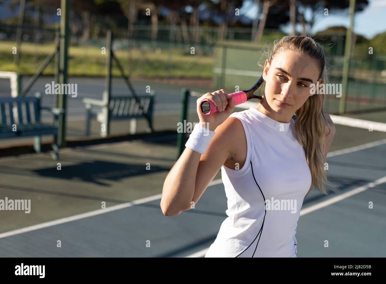 Jeune femme confiante de tennis caucasien avec raquette autour du cou sur le court le jour ensoleillé Banque D'Images