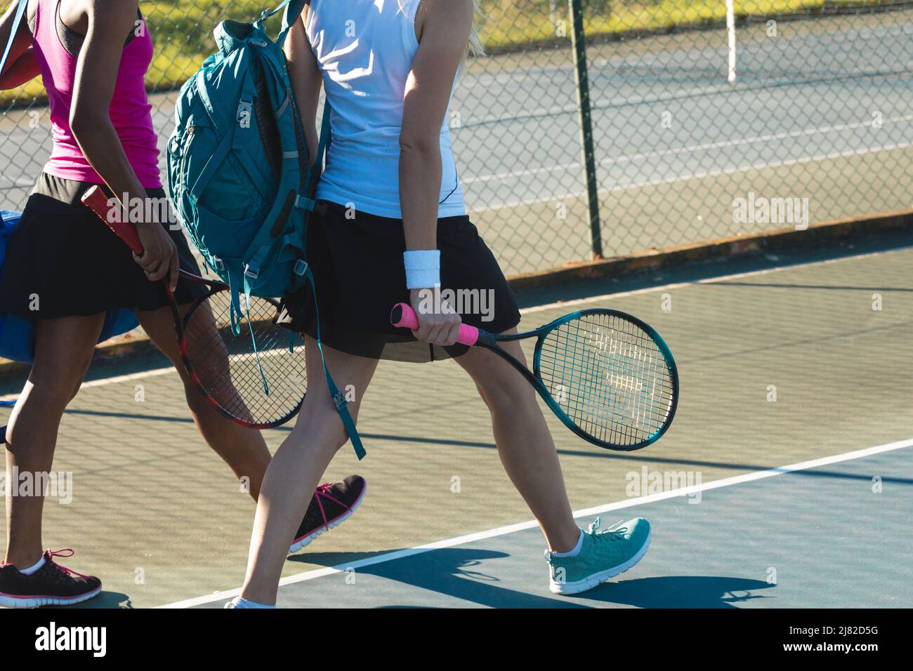 Une partie basse de joueuses multiraciales marchant avec des sacs à dos et des raquettes sur le court de tennis Banque D'Images