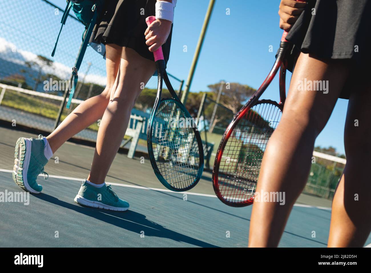 Une partie basse de joueuses de tennis multiraciales marchant des raquettes sur le court le jour ensoleillé Banque D'Images