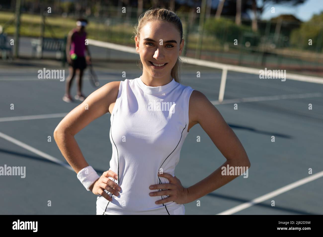 Portrait d'une belle femme de tennis caucasienne souriante debout avec les mains sur la hanche sur le court Banque D'Images