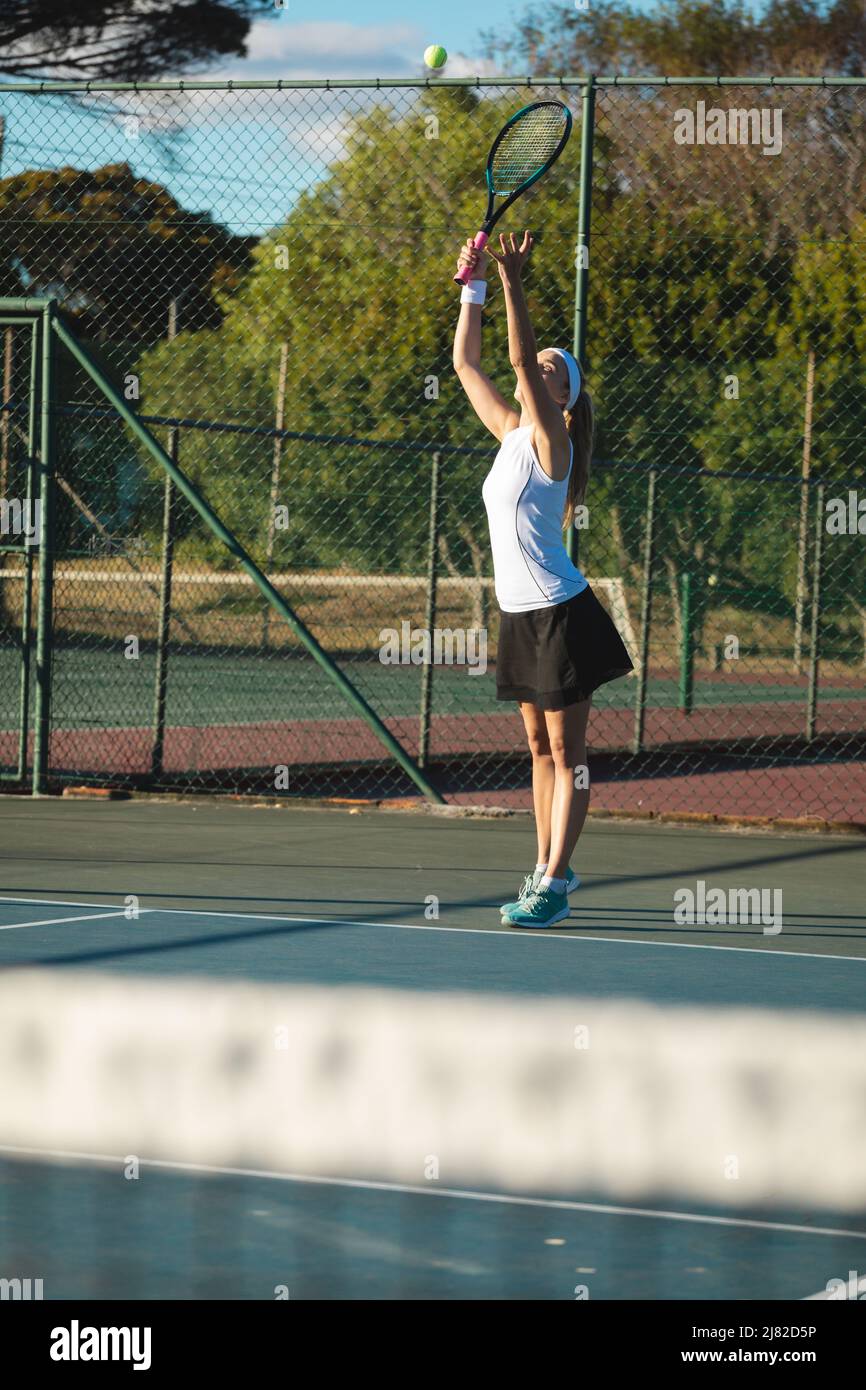 Pleine longueur de jeune femme caucasienne servant sur le court de tennis le jour ensoleillé Banque D'Images