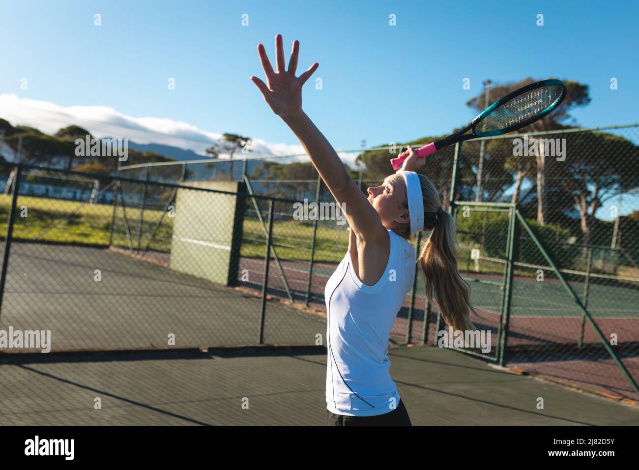 Vue latérale d'une jeune femme caucasienne servant sur le court de tennis par beau temps Banque D'Images