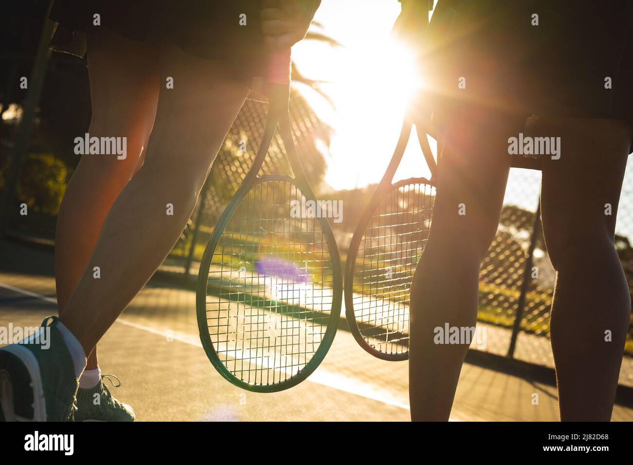 Jeunes filles de tennis multiracial éclairées marchant avec des raquettes sur le court Banque D'Images