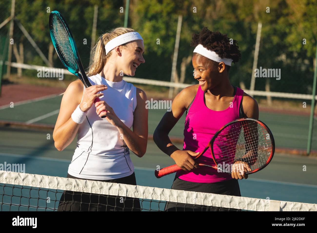 De jeunes joueuses de tennis multiraciales ravie en parlant tout en tenant des raquettes debout sur le court Banque D'Images
