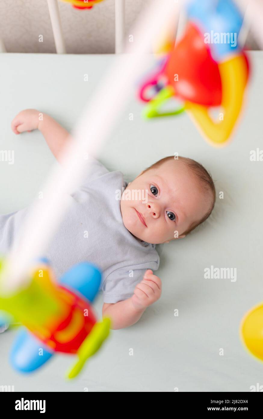 Le bébé regarde le mobile couché dans le berceau . Mobile au lit de bébé. Un article sur les loisirs pour enfants. Les mains de maman sont libres. Un article sur le choix d'un mobile dans le berceau. Le bébé a 0-3 mois. Un bébé Banque D'Images