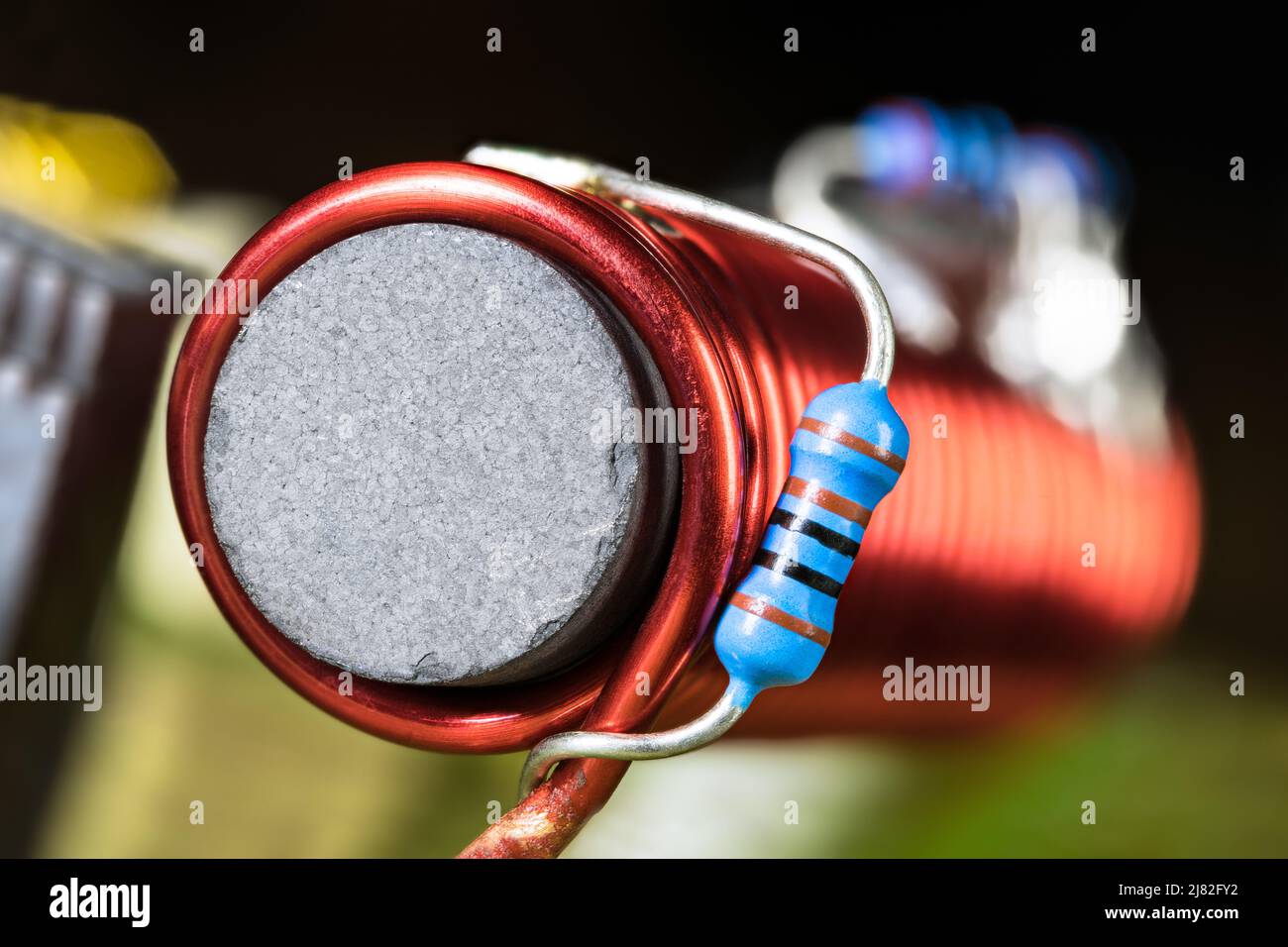 Inductance cylindrique avec noyau ferromagnétique noir enveloppée par un fil rouge sur le détail de ci. Gros plan de petites résistances en carbone bleu soudées sur l'enroulement de bobine. Banque D'Images