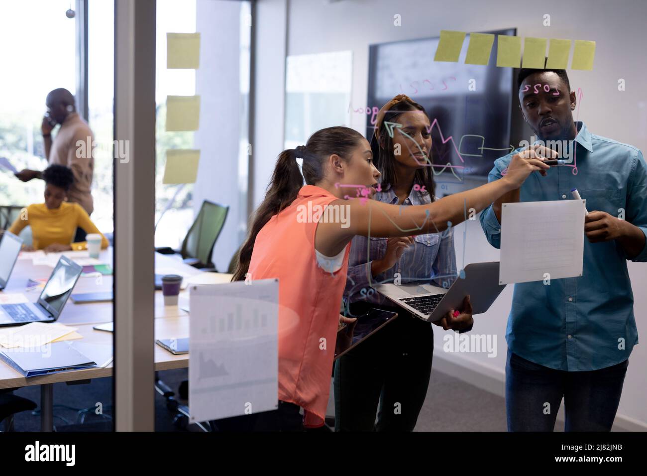 De jeunes conseillers multiraciaux, hommes et femmes, discutent de la stratégie au-dessus d'un mur de verre dans la salle de réunion Banque D'Images