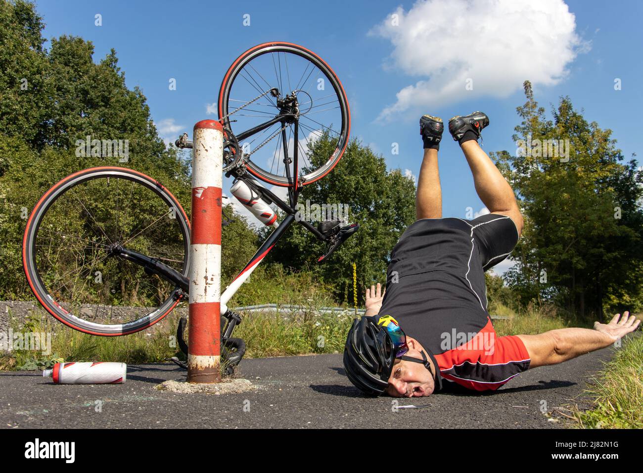 Le cycliste malheureux tombe du vélo à côté de la barrière sur une piste cyclable. Banque D'Images