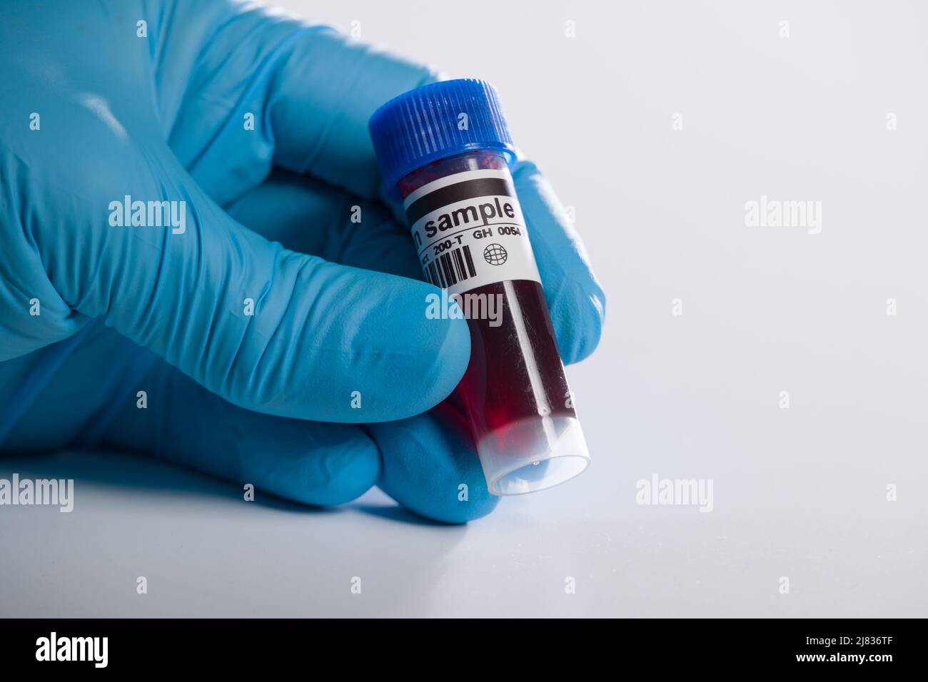 gros plan d'une main dans des gants médicaux manipulant une sonde sanguine avec des informations codées Banque D'Images