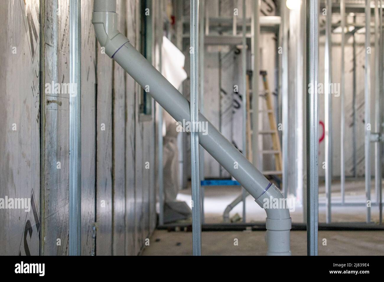 Un tuyau en PVC gris est intégré diagonalement à travers le cadre en acier galvanisé derrière les murs d'un nouveau bâtiment Banque D'Images