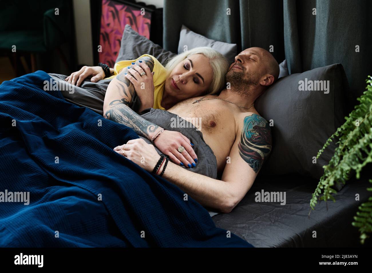 Tatoué homme et femme caucasiens matures dans l'amour dormant ensemble dans le lit à la maison le matin Banque D'Images