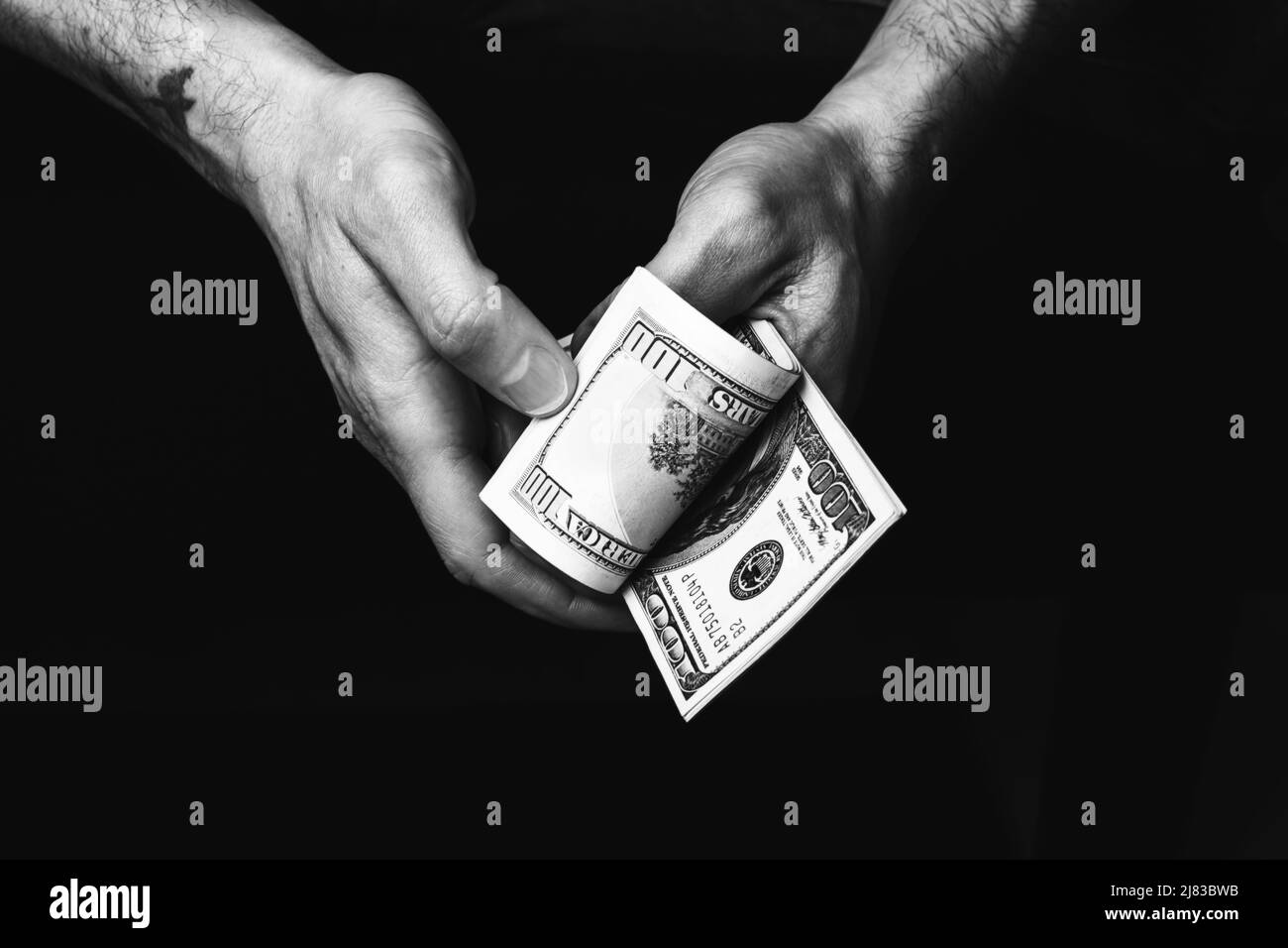 Des mains de sexe masculin nous tiennent des billets de cent dollars. Un homme avec de l'argent américain en gros plan. Photo en noir et blanc Banque D'Images