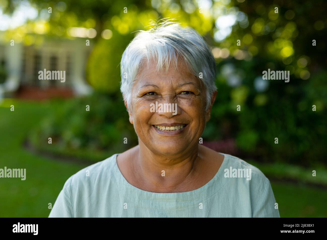 Portrait en gros plan d'une femme biraciale souriante avec de courts cheveux gris contre les arbres dans le parc Banque D'Images