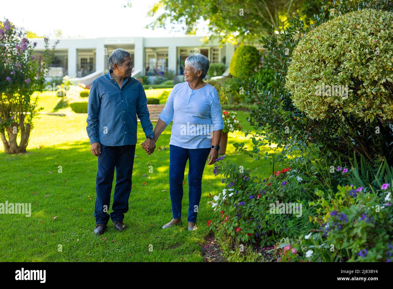 Couple senior souriant et biracial tenant les mains et debout sur une terre herbeuse dans le parc Banque D'Images