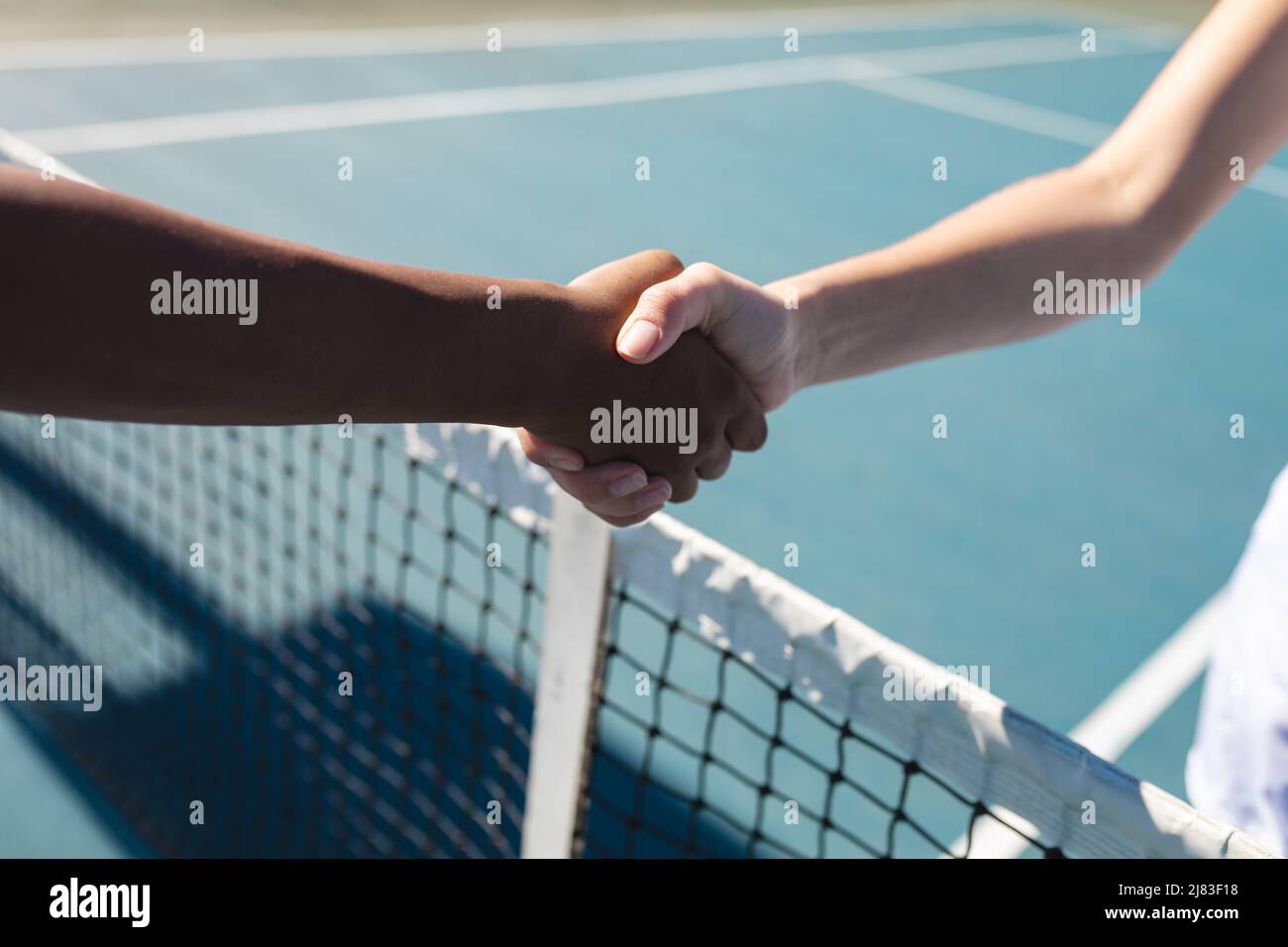 Les mains de femmes de tennis biracial coupées avec poignée de main sur le filet sur le court le jour ensoleillé Banque D'Images