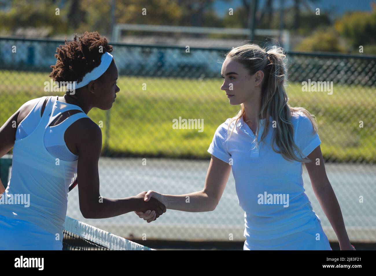 Des jeunes filles de tennis multiraciales confiantes se font poignée de main sur le terrain par beau temps Banque D'Images
