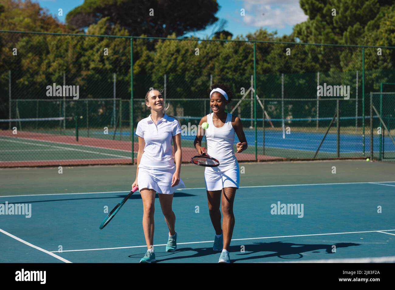 Une femme biraciale souriante double l'équipe de marche sur le court de tennis par beau temps Banque D'Images