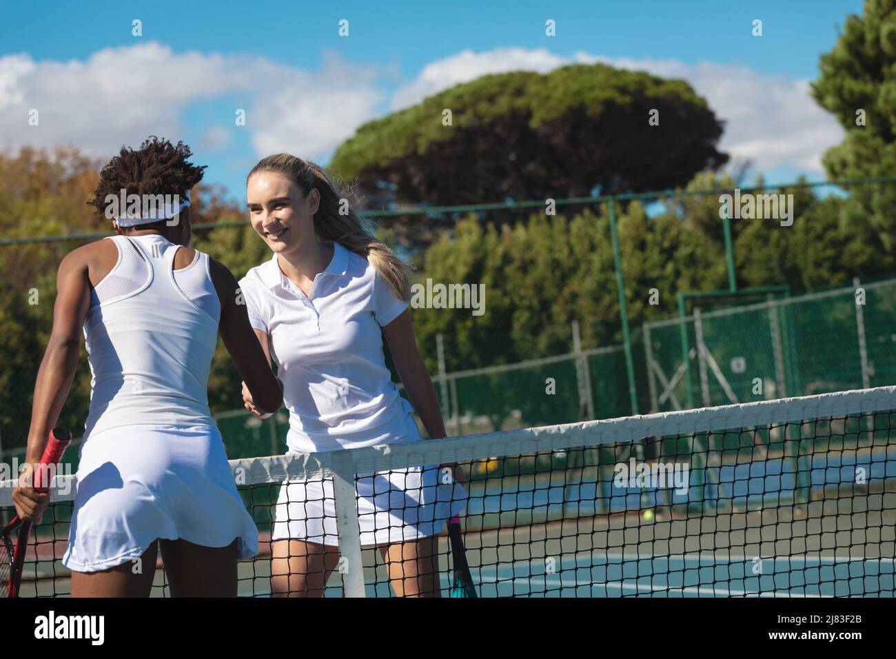 Souriante joueuse de tennis caucasienne se serrant la main avec un concurrent afro-américain sur le terrain Banque D'Images