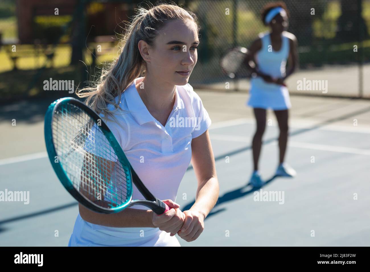 Belle jeune femme caucasienne joueuse avec un partenaire afro-américain sur le court de tennis Banque D'Images