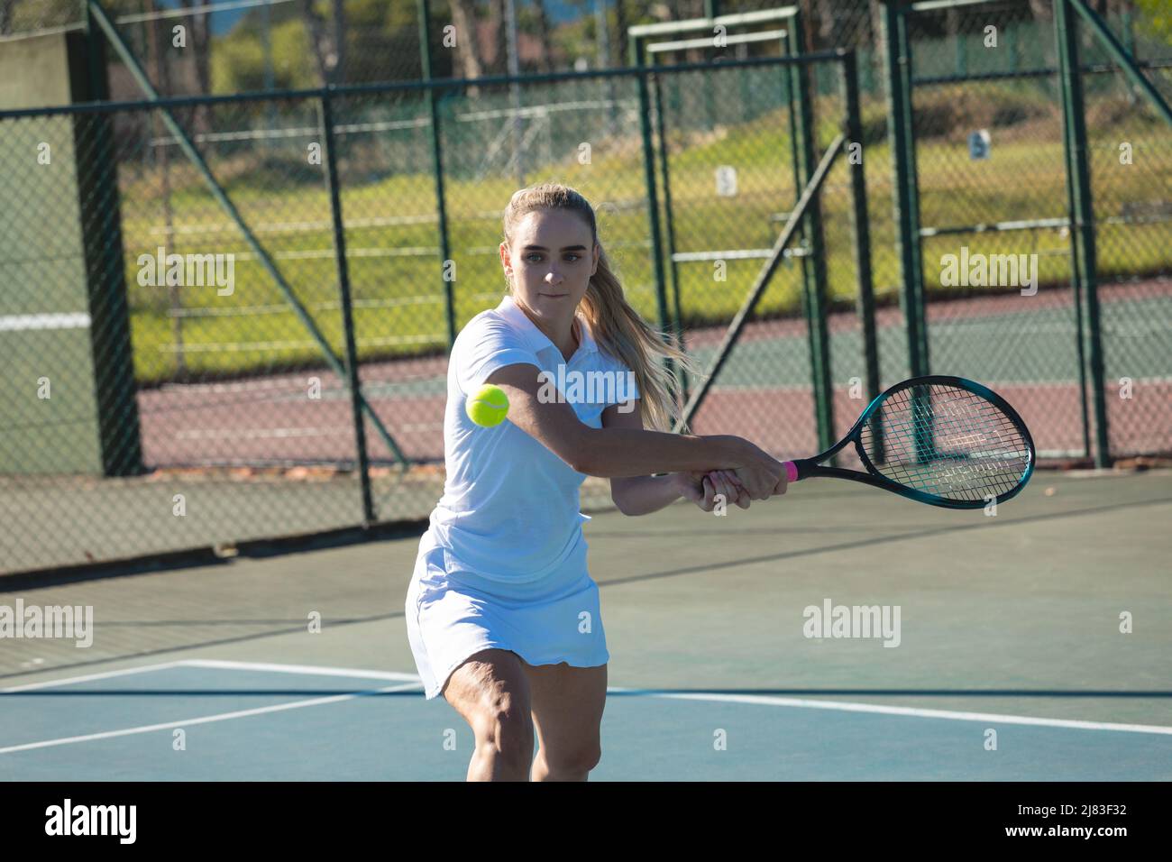 Belle jeune femme caucasienne joueur frapper balle de tennis avec raquette sur le court le jour ensoleillé Banque D'Images