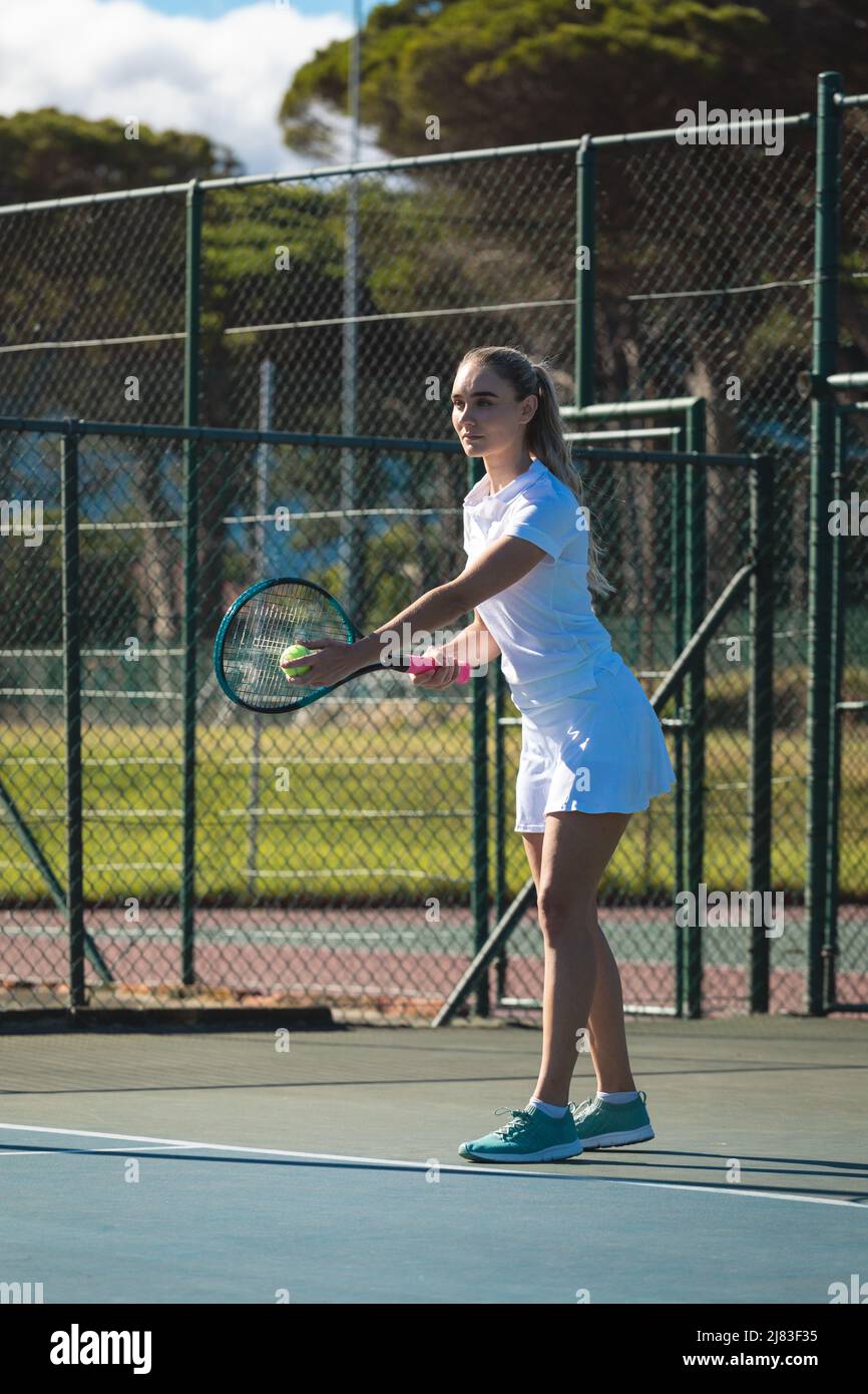 Jeune femme confiante de race blanche servant une balle de tennis avec raquette sur le court par beau temps Banque D'Images