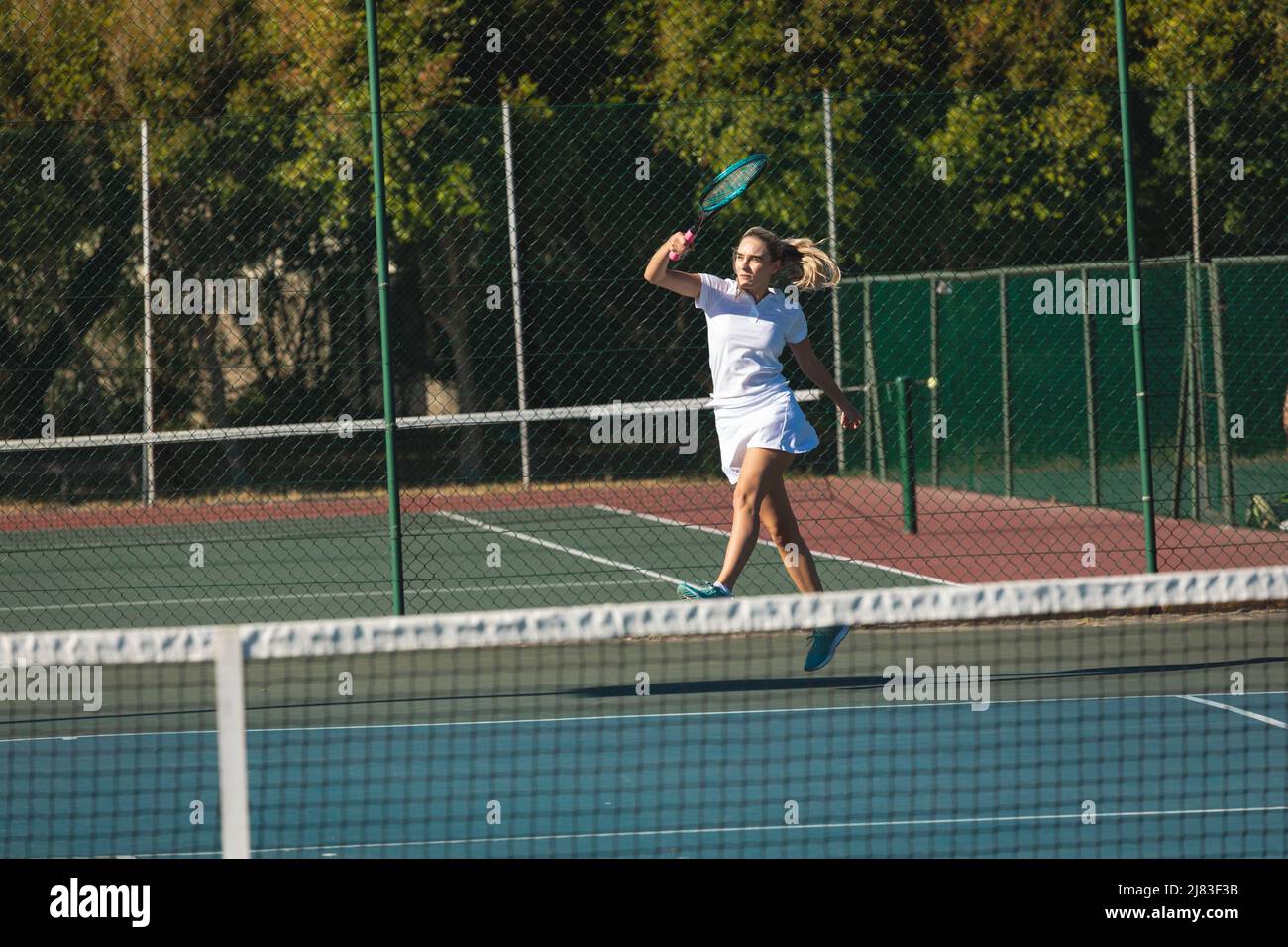 Une jeune femme de race blanche sautant en jouant au tennis sur le terrain par beau temps Banque D'Images