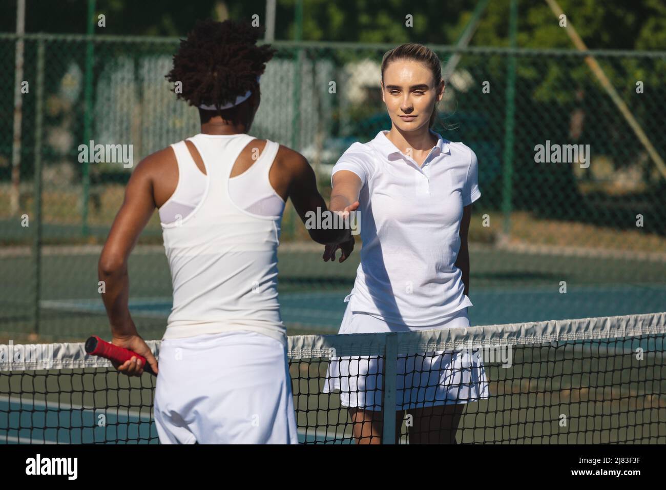 Une joueuse caucasienne se serrer la main sur le net avec des concurrents afro-américains sur le court de tennis Banque D'Images