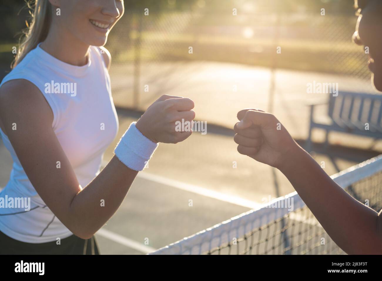 Les jeunes joueuses de tennis multiraciales souriantes donnent une bosse de poing sur le filet sur le terrain Banque D'Images