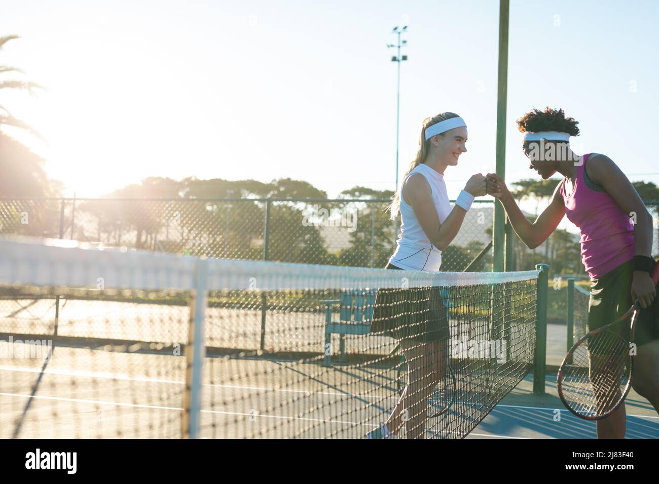 Jeunes joueuses de tennis multiraciales heureuses donnant le poing sur le filet sur le court Banque D'Images