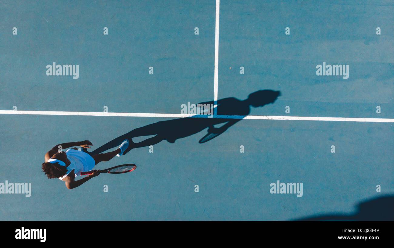 Vue en hauteur d'une jeune joueuse de tennis afro-américaine avec des jeux d'ombre sur un terrain bleu Banque D'Images