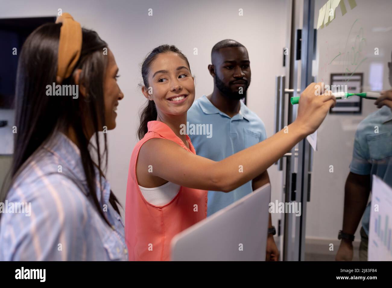 Jeune femme d'affaires hispanique souriante, écrivant une stratégie avec des collègues biraciaux dans la salle de conférence Banque D'Images