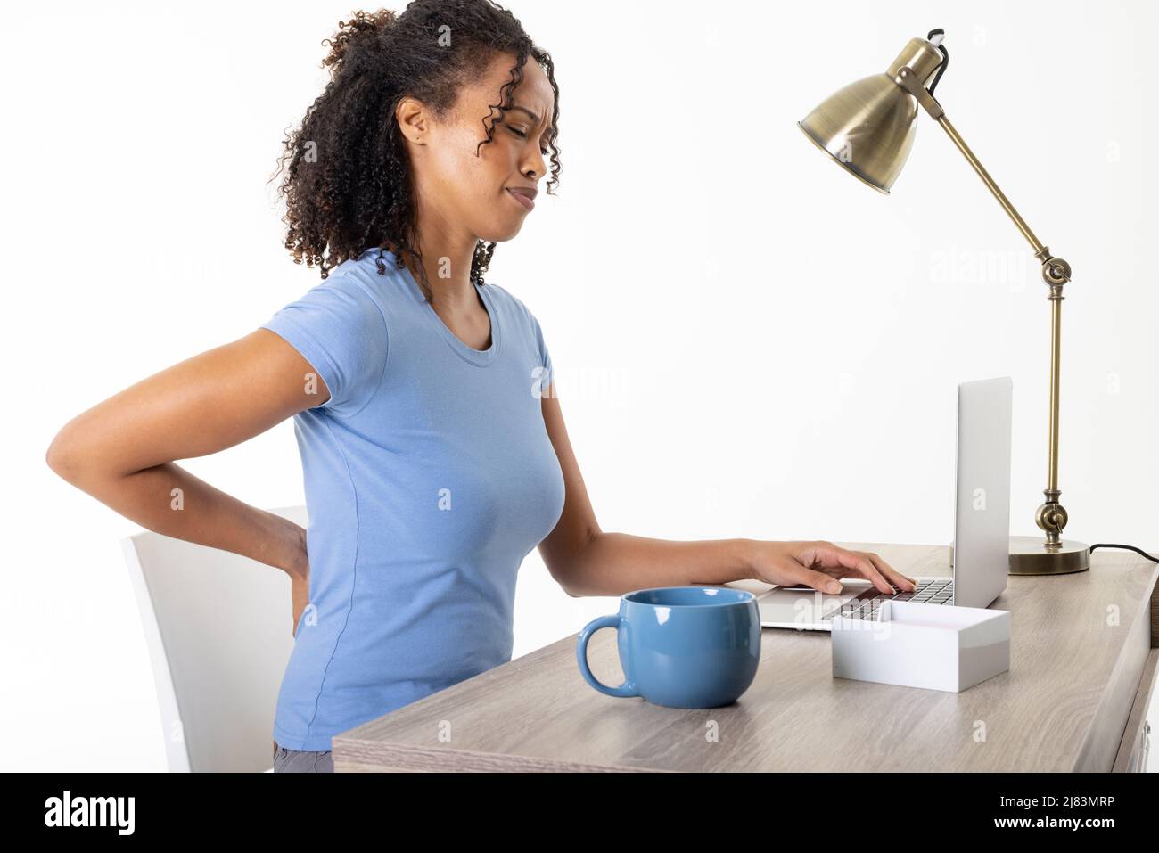 Afro-américaine femme adulte de taille moyenne avec mal de dos en utilisant un ordinateur portable par tasse et lampe sur table, espace de copie Banque D'Images