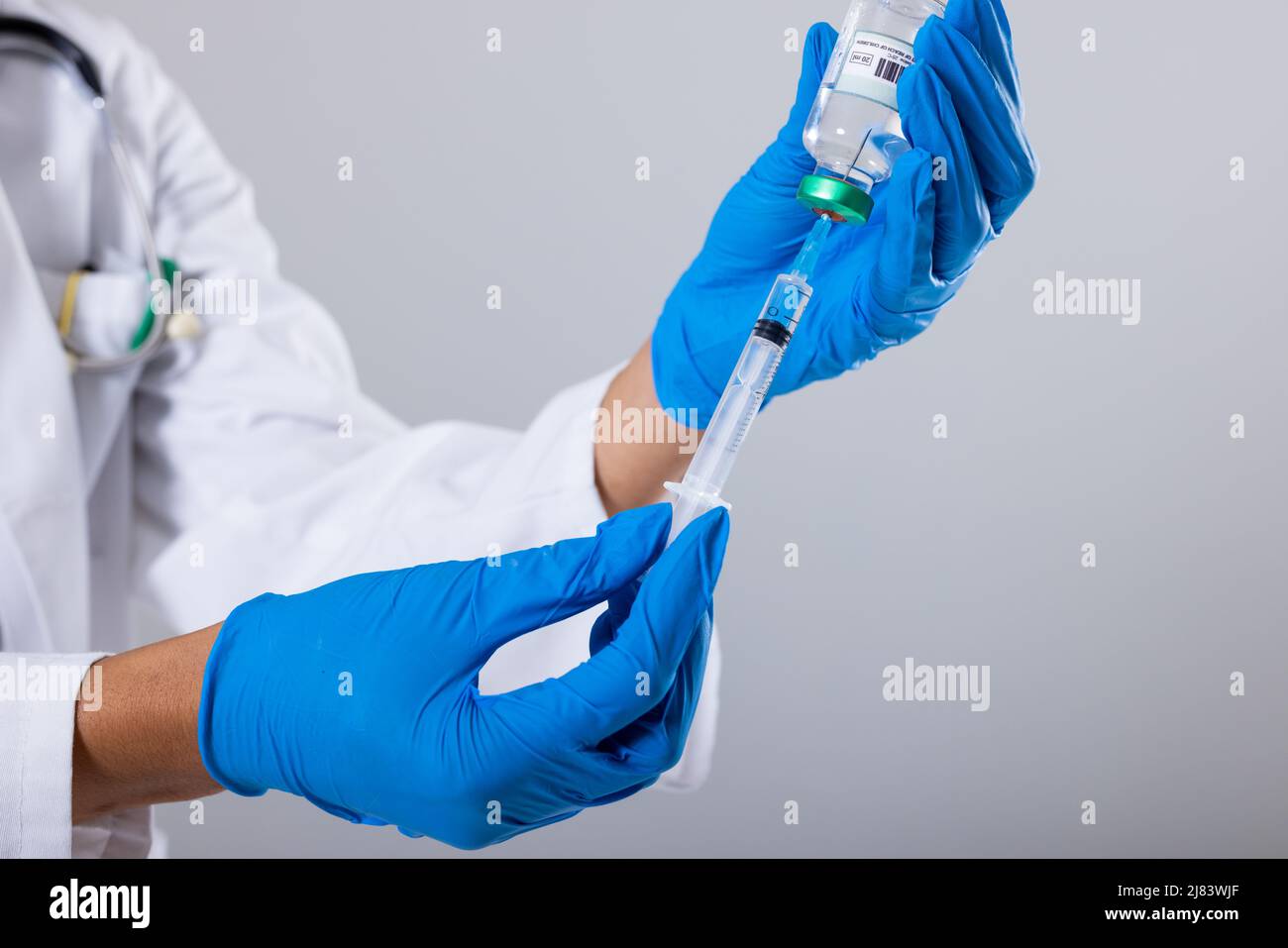 Section médiane d'une femme afro-américaine de sexe moyen, médecin, portant des gants tenant un flacon et une seringue Banque D'Images