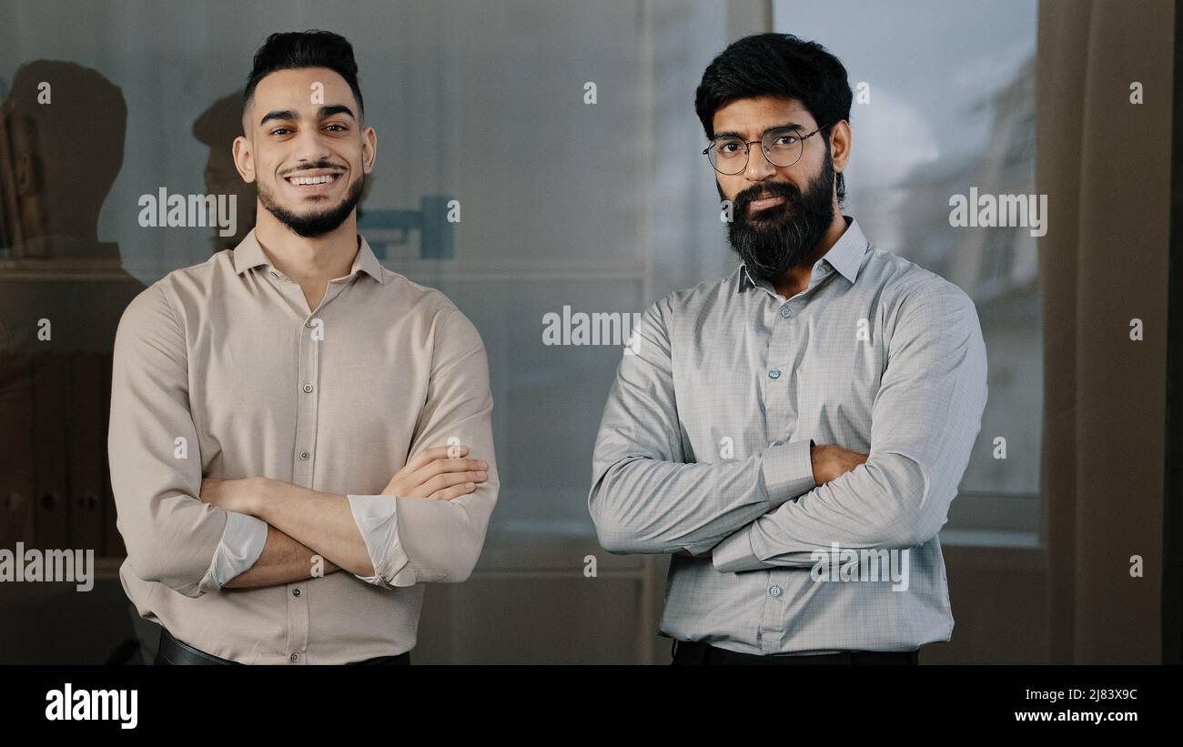 Deux amis multiraciaux divers collègues partenaires d'affaires hispanique homme arabe barbu gars debout dans le bureau posant avec les bras croisés hochant la tête Banque D'Images