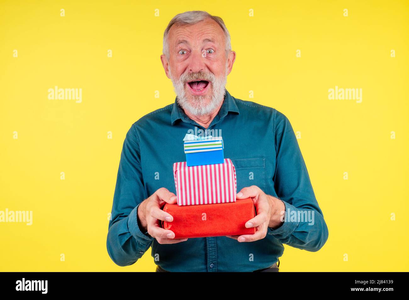 portrait stupéfié caucasien vieux homme âgé tenant deux boxex de cadeaux dans le fond jaune de studio Banque D'Images