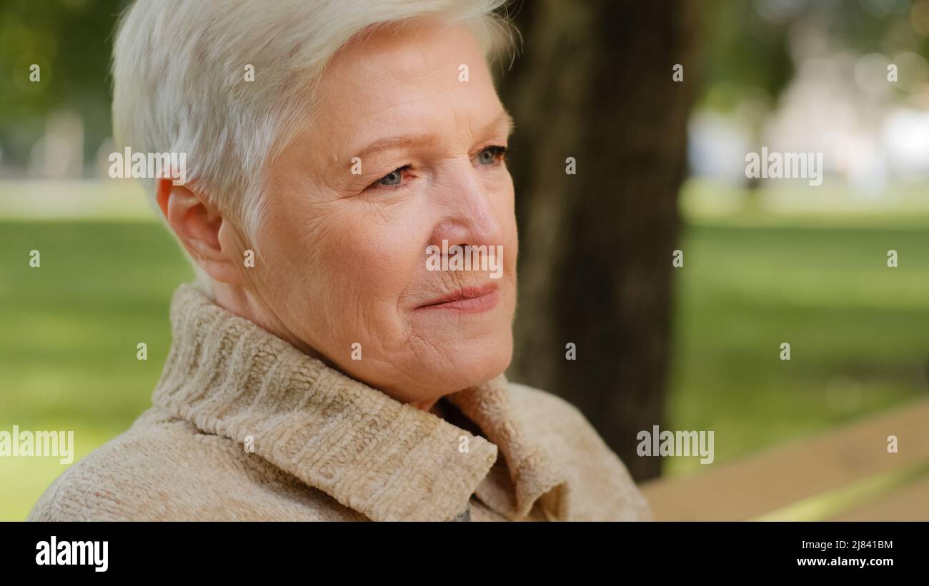 Gros plan portrait d'une femme heureuse et âgée belle regardant l'appareil photo se détendre en posant dehors par temps frais, souriante femme âgée sentiment de dame âgée Banque D'Images