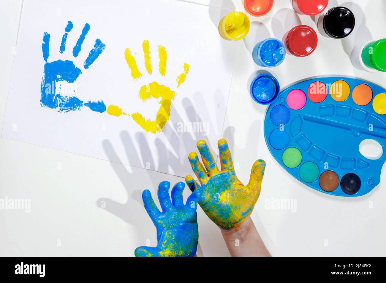 Empreintes pour enfants. Les palmiers bleus et jaunes sont imprimés sur une feuille de papier blanche, les mains des enfants dans la peinture, une palette de peintures colorées, la gouache. Haut vi Banque D'Images