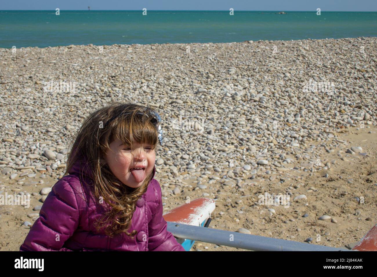 Adorable petite fille assise sur un bateau au bord de la mer pendant un voyage en Italie jouant à faire des visages. Banque D'Images