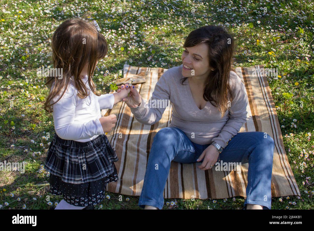 Adorable petite fille donnant des pâquerettes à sa mère qui est assise sur un pré de fleurs pendant un séjour en Italie Banque D'Images