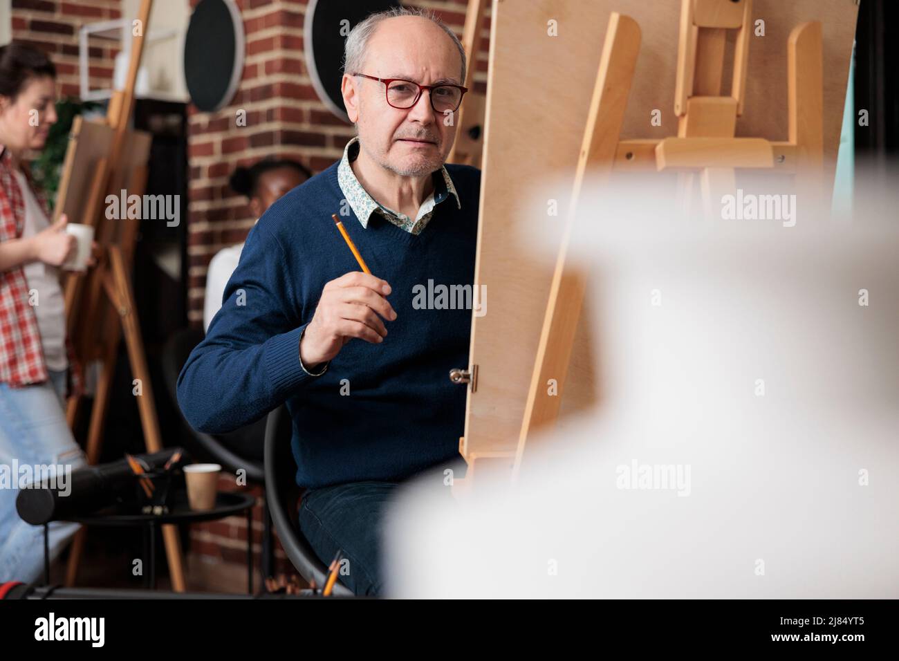 Portrait d'un étudiant senior assis en classe d'art devant sur toile dessin modèle de vase à l'aide d'un crayon graphique. Équipe diversifiée travaillant à la technique d'esquisse développant des compétences artistiques. Concept créatif Banque D'Images