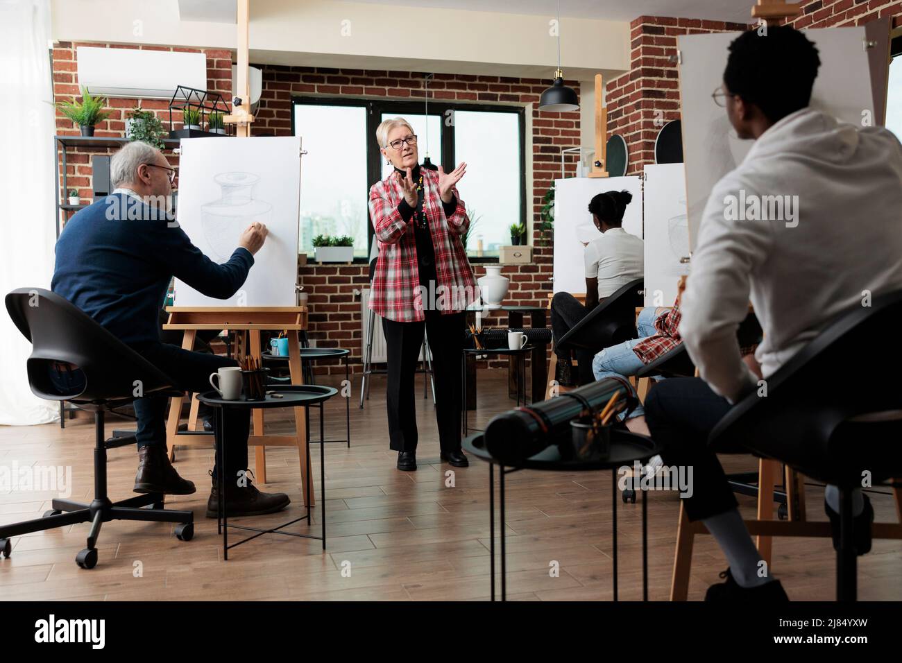 Professeur d'art expliquant la technique de dessin à une équipe diversifiée pendant la leçon d'art. Les personnes multiethniques dessinant un vase croquis sur toile à l'aide d'un crayon graphique travaillant sur l'illustration artistique. Concept de passe-temps créatif Banque D'Images